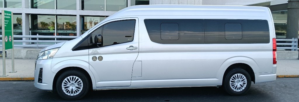 Toyota Hiace plateada de Torote Luxury Transportation en zona de descenso de pasajeros.